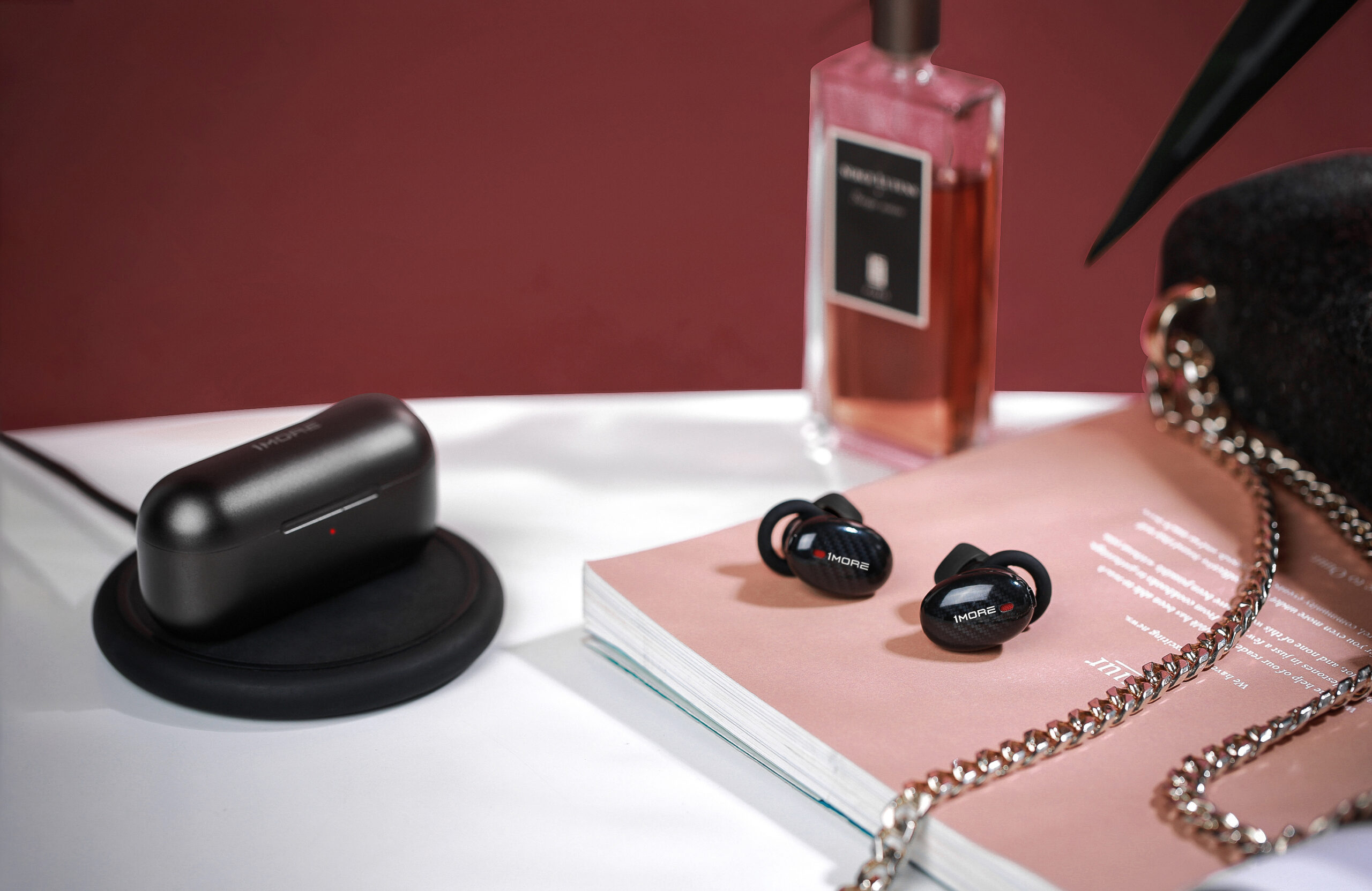 1MORE's true wireless ANC headphones on a table with perfume, notebook and purse